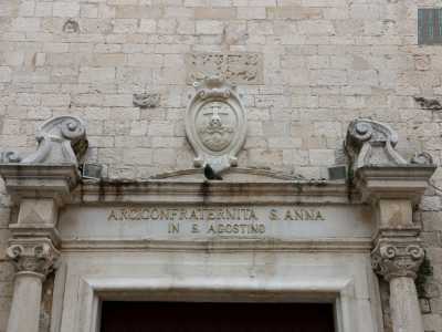 La porta d'accesso � racchiusa da un architrave originario, al di sopra del quale si erge un teschio, simbolo dell'arciconfraternita di San Marco della Buona Morte. Un�epigrafe invece ricorda quando la chiesa fu gestita dai nobili lombardi giunti a Bari al seguito di Iabella d�Aragona e Bona Sforza, assumendo il nome di Sant�Ambrogio prima e Sant'Agostino poi, con il subentro dei monaci devoti all'Ipponate